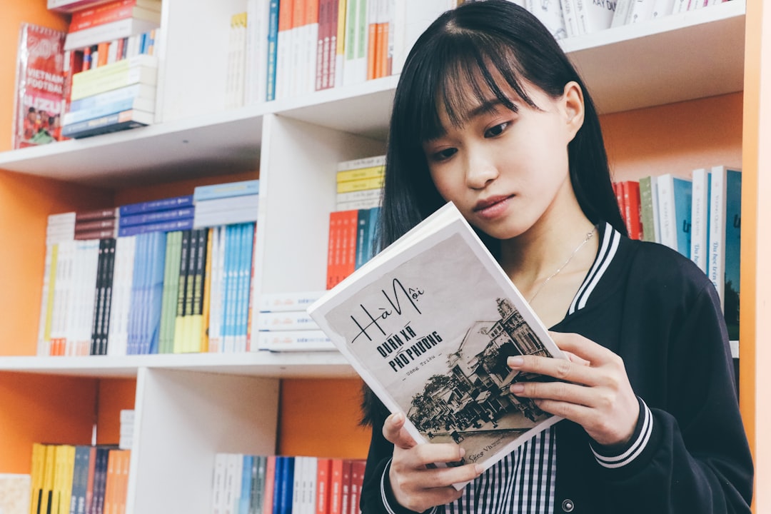 a woman reading a book in front of a bookshelf